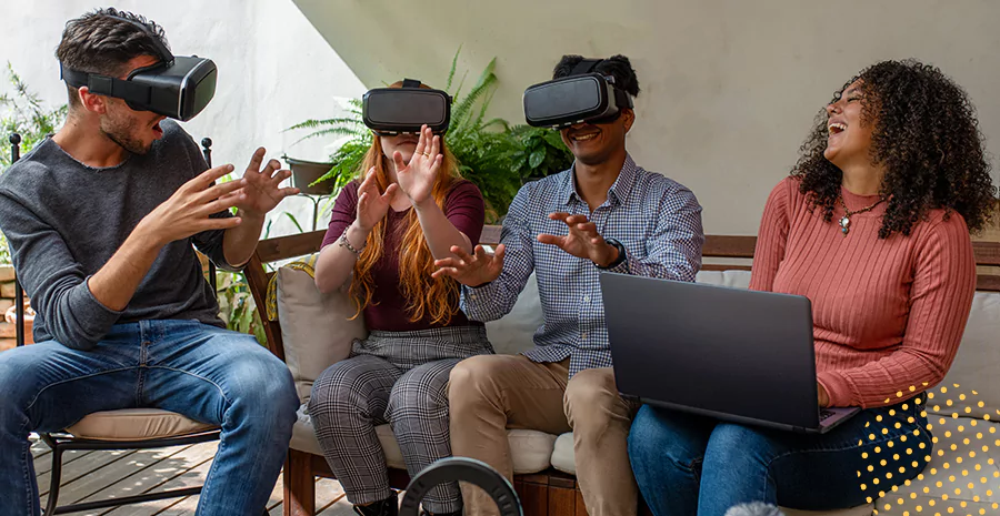 imagem de três pessoas sentadas usando óculos de realidade virtual e outra mulher sentada rindo segurando um computador no colo