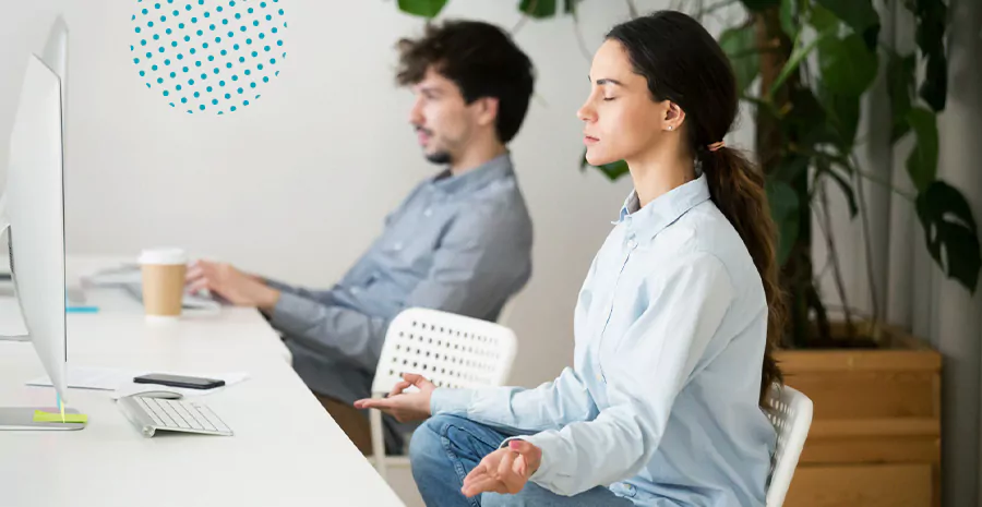 imagem de uma mulher sentada fazendo meditação com outro homem sentado ao seu lado mexendo em um computador