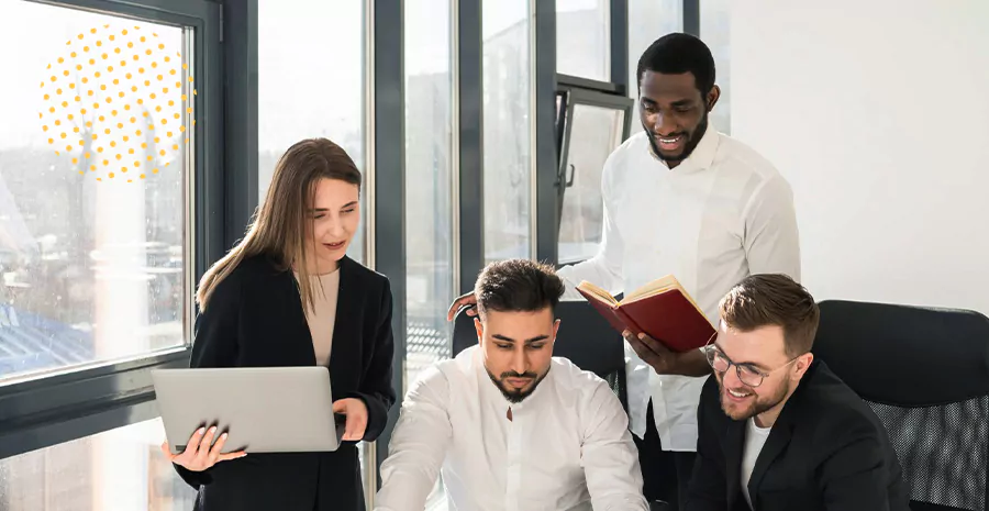 imagem de três homens e uma mulher de frente para uma mesa olhando papéis espalhados nela