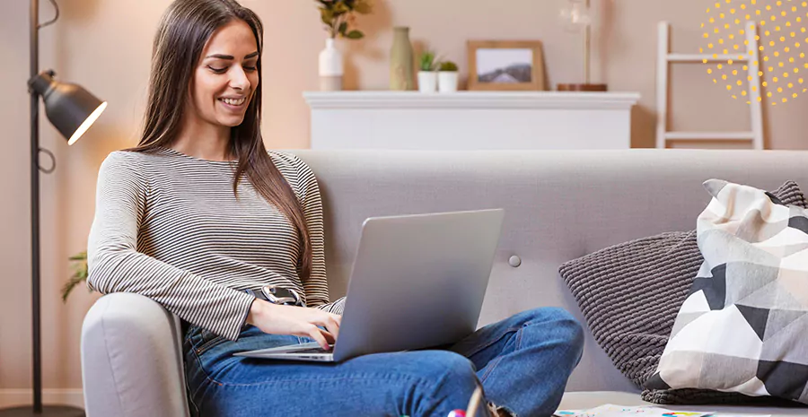 imagem de uma mulher sorrindo sentada em um sofá e mexendo em um computador