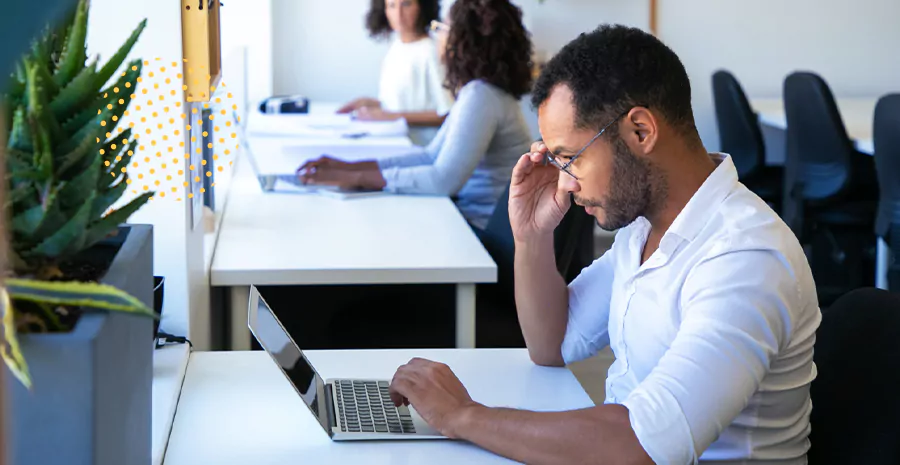 imagem de um homem sentado na frente de um computador colocando a mão no rosto