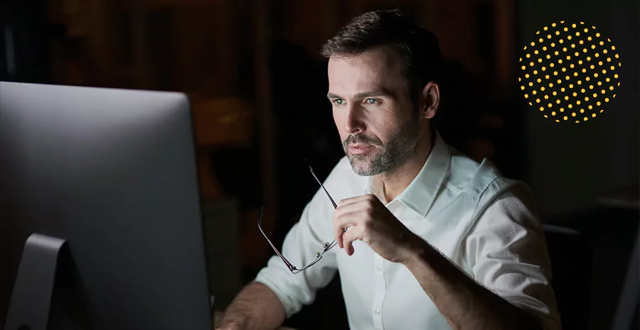 imagem de um homem sentado na frente de um computador segurando um óculos