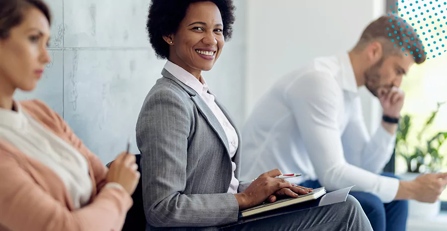 imagem de uma mulher sentada sorrindo com um caderno no colo ao lado de outra mulher e um homem sentados