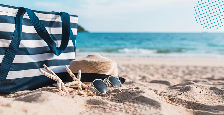 imagem de uma praia com foco em um chapéu e uma bolsa listrada na areia