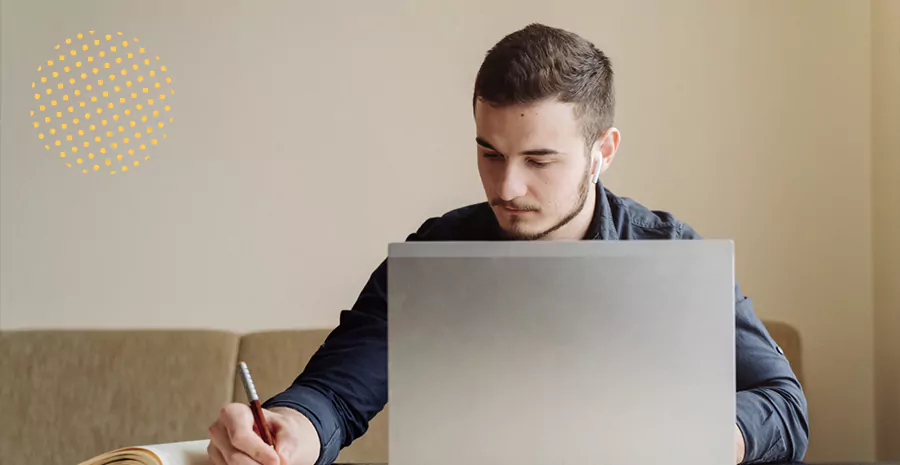 imagem de um homem sentado na frente de um computador e escrevendo em um caderno