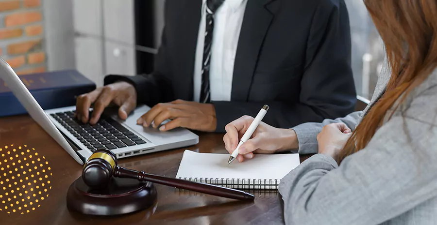 imagem de uma mulher sentada escrevendo em um caderno e um homem sentado ao seu lado mexendo em um computador