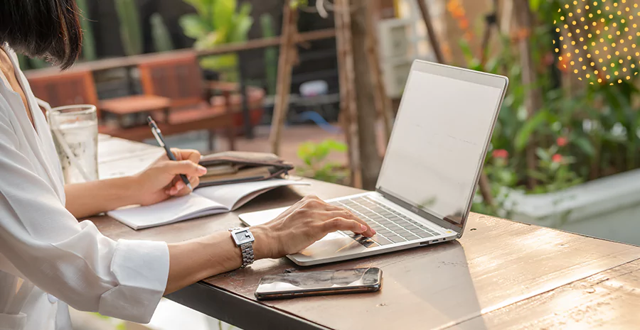 Uma mulher teclando em um notebook e anotando em um caderno