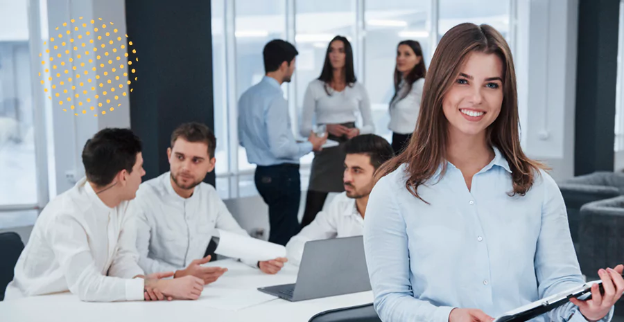 Uma mulher sorrindo e um grupo de funcionários conversando ao fundo