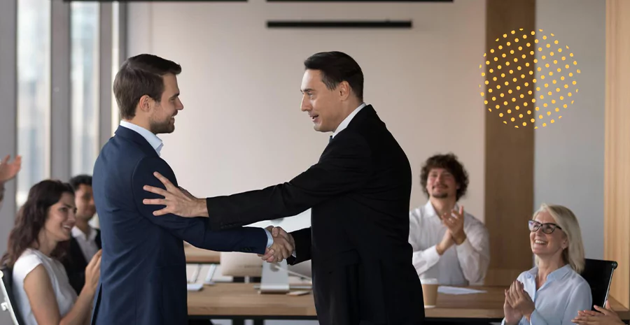 Dois homens apertando as mãos em frente a uma plateia em uma sala de reunião