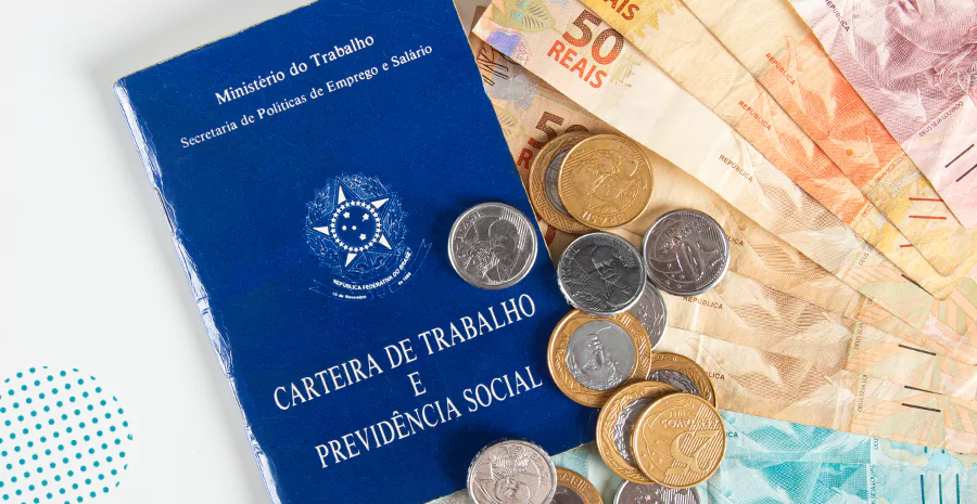 Carteira de trabalho ao lado de cédulas e moedas de reais