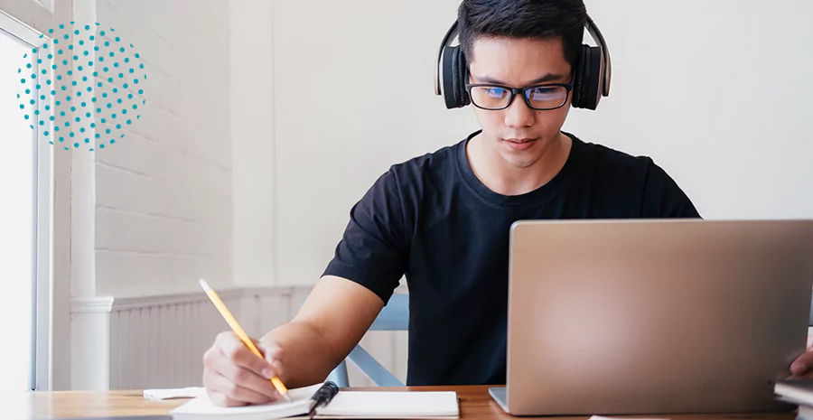 Homem escrevendo enquanto observa um notebook, imagem representa uma pessoa autodidata