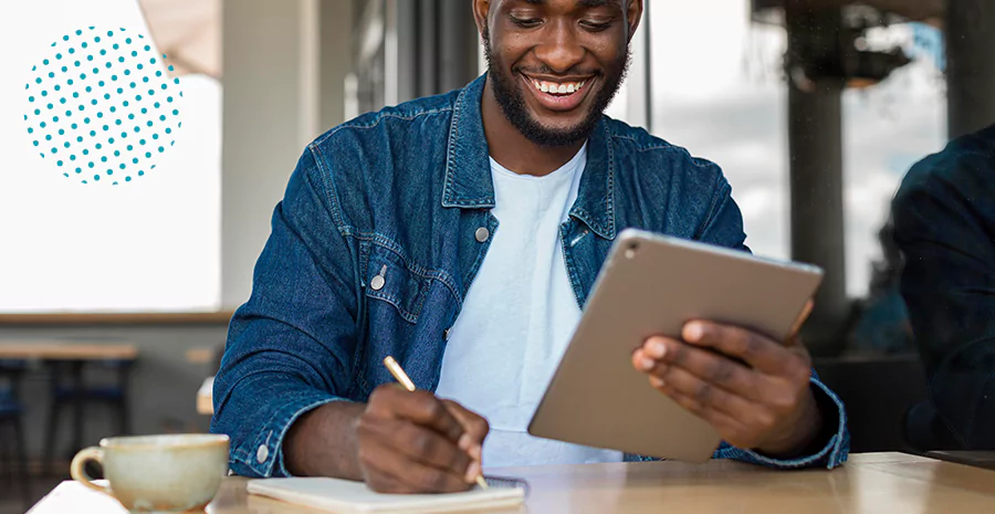 Homem escrevendo enquanto segura um tablet, representando uma pessoa autodidata