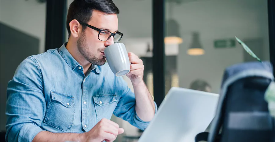 Homem tomando café enquanto utilizando o computador