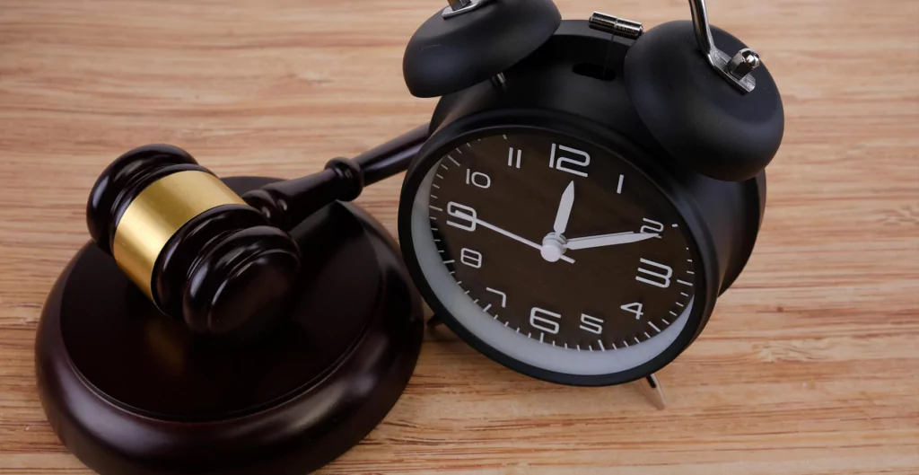 Relógio preto ao lado de um martelo de justiça