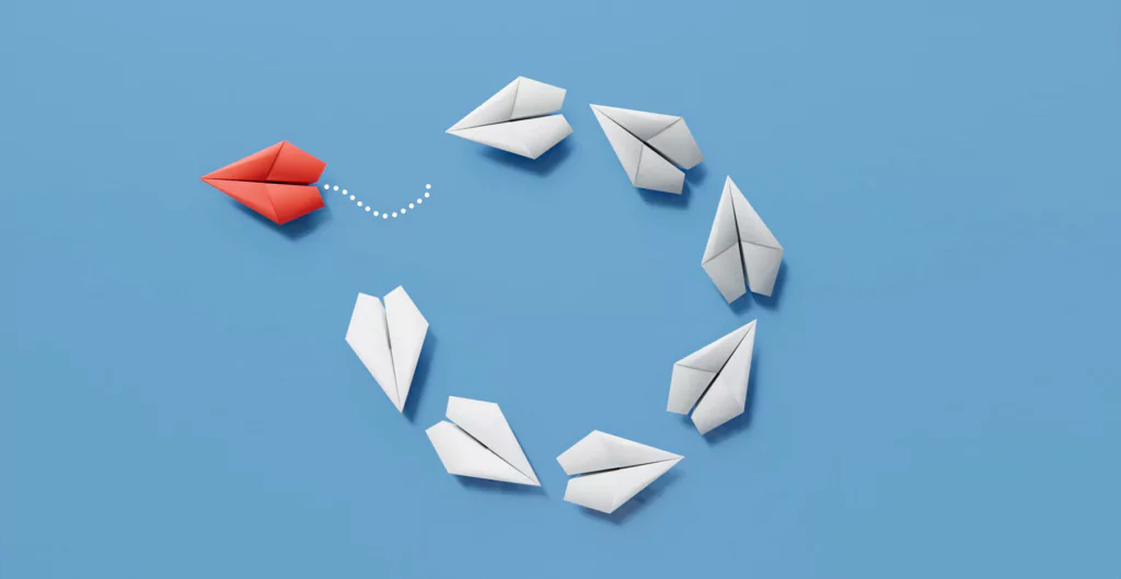 Avião de papel vermelho se distanciando de um círculo de aviões de papeis brancos