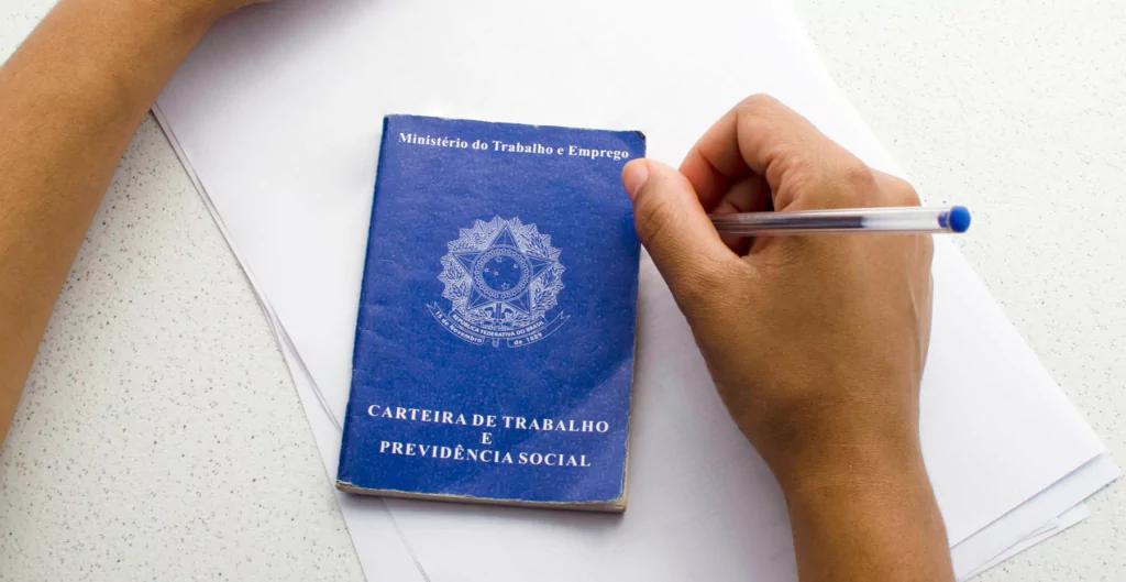 Uma pessoa segurando uma caneta e anotando em uma carteira de trabalho