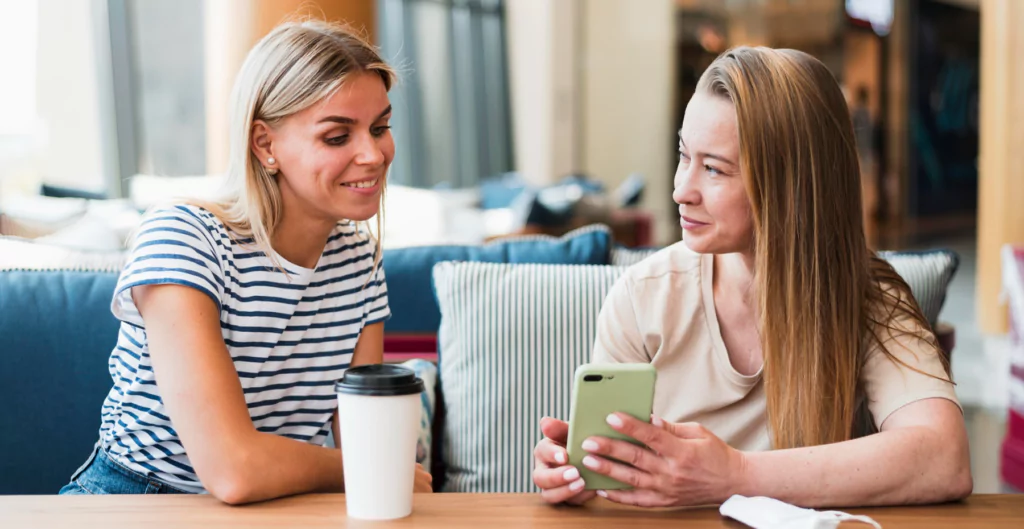 Duas mulheres sentadas à mesa olhando para seus telefones celulares