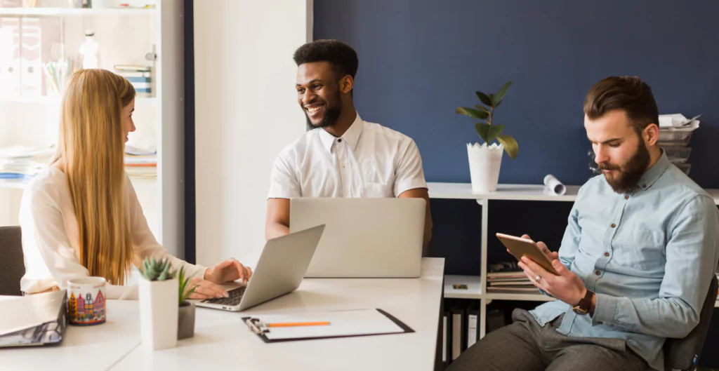 Três pessoas sentadas à mesa com laptops