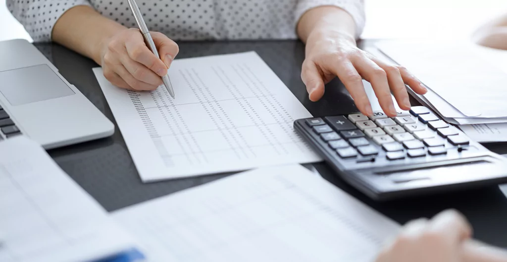 Uma pessoa usando uma calculadora e caneta para fazer papelada