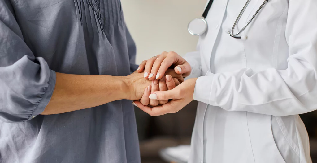 imagem mostra uma médica e um paciente de mãos dadas