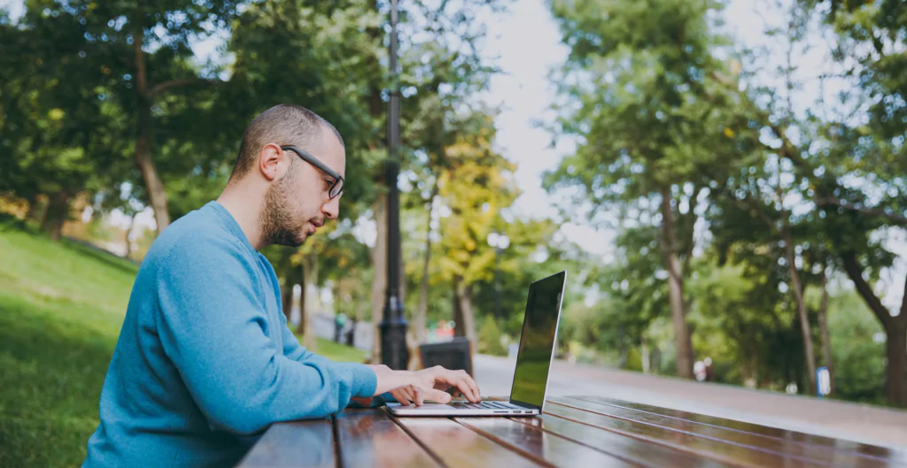 homem sentado de frente para um notebook em um parque