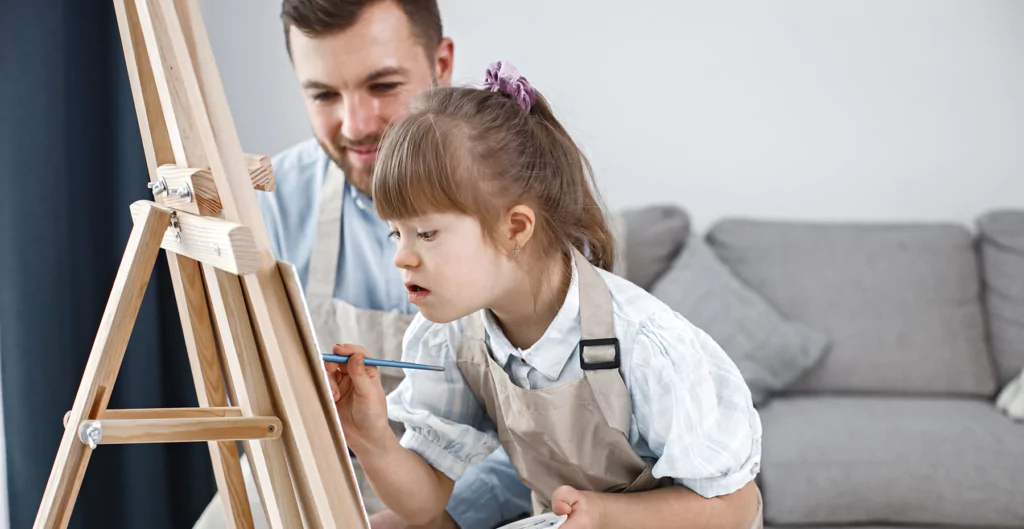 imagem mostra uma criança pintando um quadro com seu pai