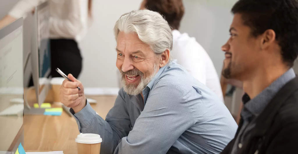 Homem idoso conversando com homem mais jovem na frente do computador
