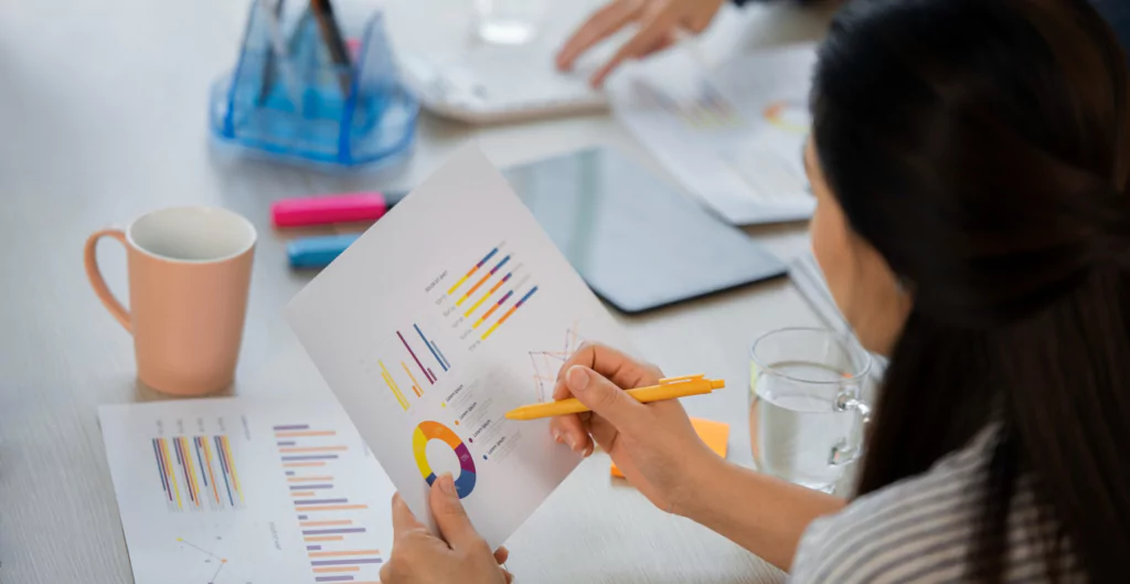 mulher fazendo anotações em uma folha com gráficos, representando o benchmarking