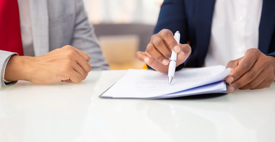 Duas pessoas conferindo um documento, sobe a mesa, utilizando uma caneta