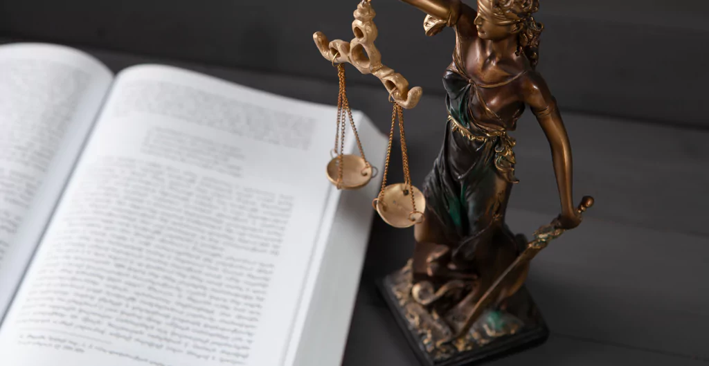 imagem mostra estátua da deusa da justiça do lado de um livro