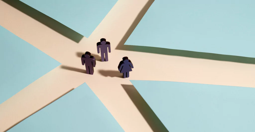 Miniaturas de pessoas em uma encruzilhada, ilustrando escolhas na carreira não linear.