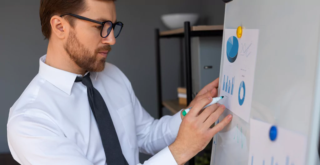 Profissional revisando gráficos em um quadro, destacando monitoramento de métricas e desempenho.