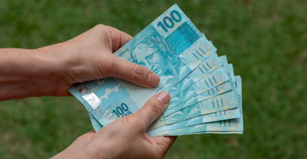 mãos segurando notas de cem reais