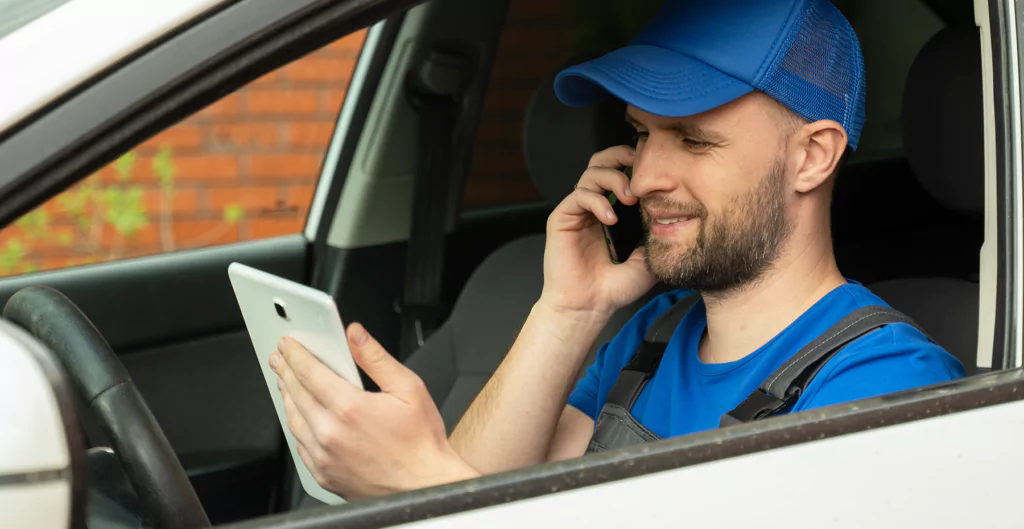 homem falando ao telefone, enquanto olha um tablet dentro do carro
