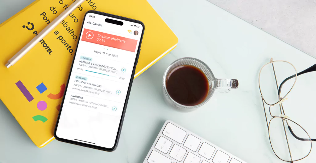 Mesa com caderneta da Pontotel, celular apresentando tela do aplicativo bate o ponto, uma xícara de café e óculos