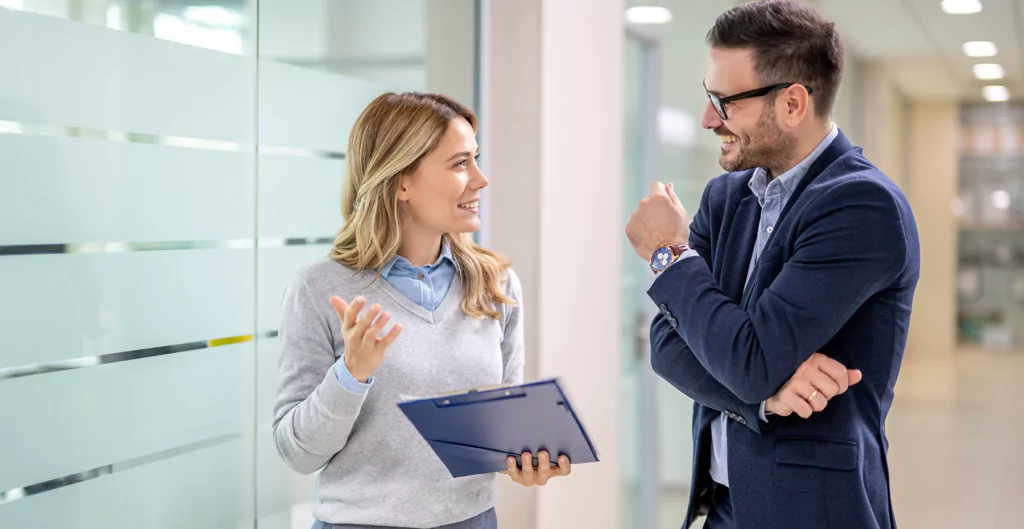 Mulher e homem conversando e sorrindo no corrido de um escritório corporativo