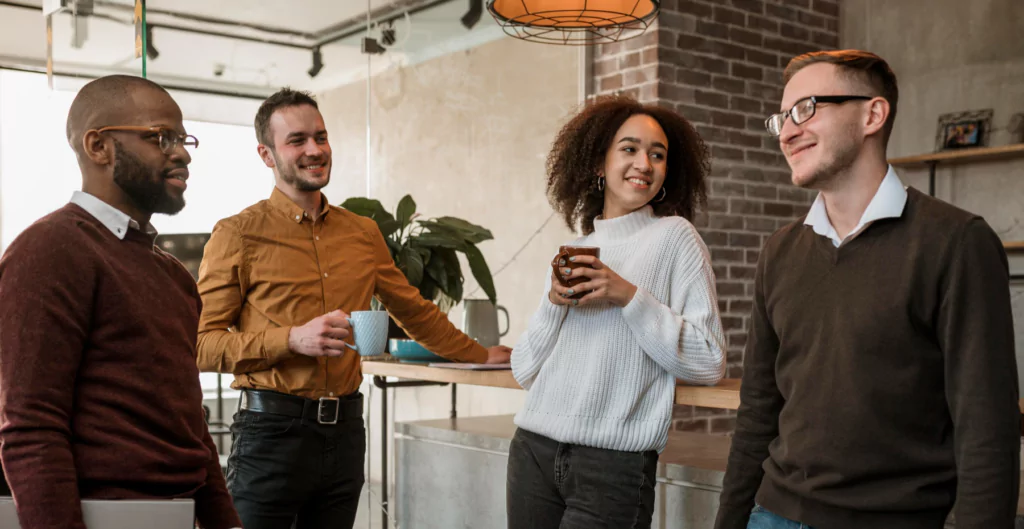 Grupo de pessoas em ambiente de trabalho conversando e se divertindo, destacando interações sociais e cooperação em equipe.