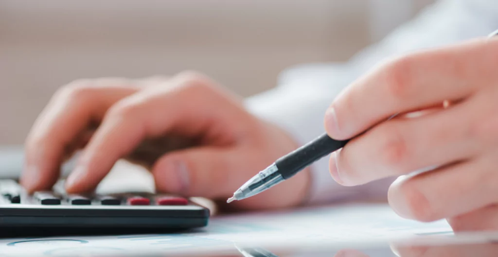 mão digitando em uma calculadora e caneta