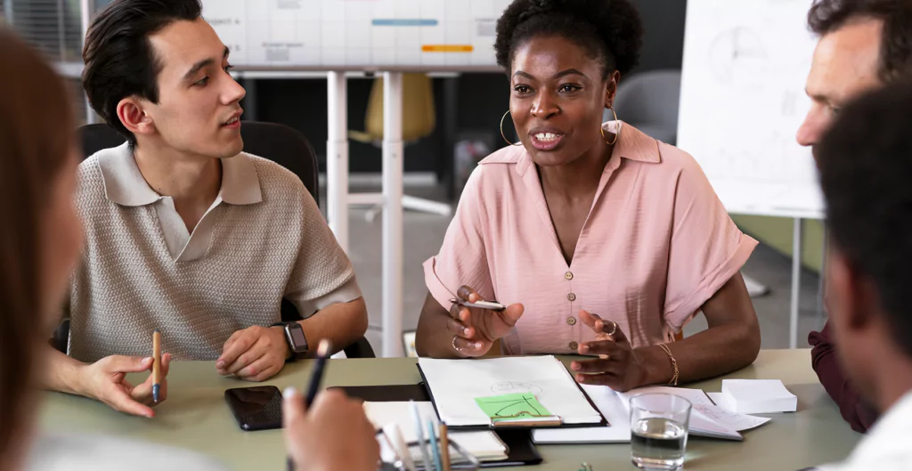 Grupo diversificado de profissionais discutindo ideias em uma reunião de trabalho. A cena retrata a colaboração e a troca de pensamentos em um ambiente de escritório moderno.