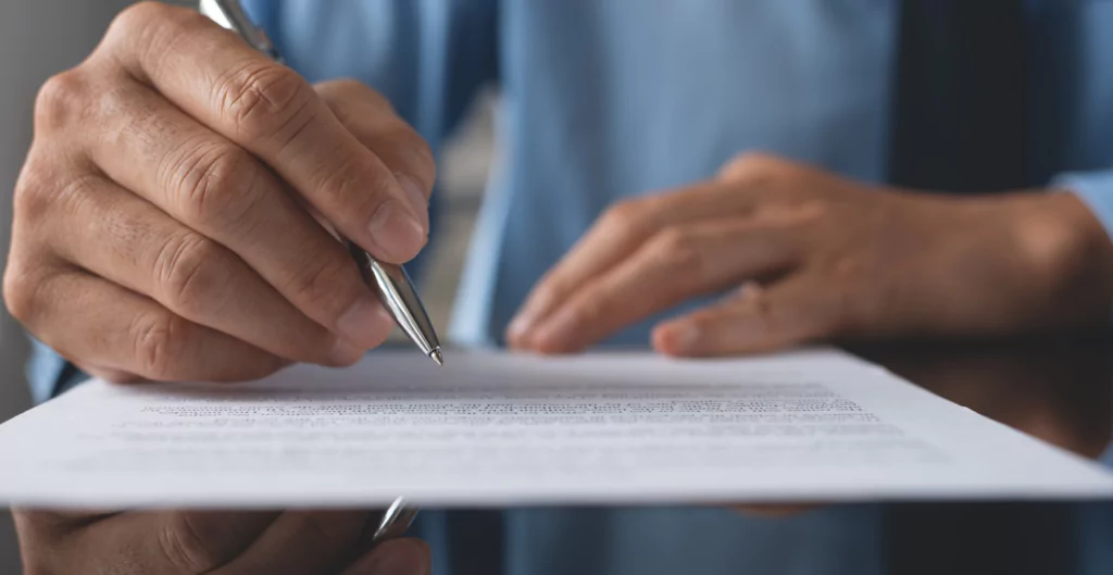 Mãos de trabalhador avulso assinando contrato em mesa de escritório com camisa azul