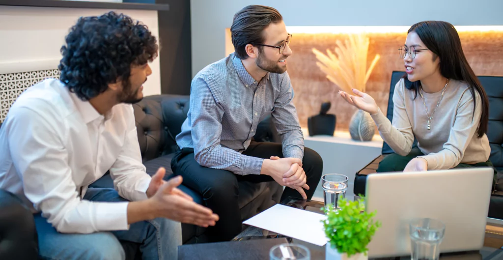 Reunião de equipe de negócios com três pessoas conversando e trocando ideias em um ambiente moderno de escritório, promovendo colaboração e inovação.
