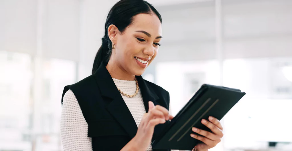 Mulher sorridente utilizando um tablet em um ambiente moderno e bem iluminado, representando a fusão entre tecnologia e estilo.