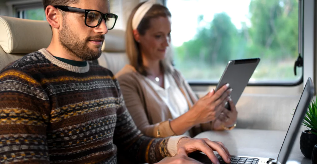 Casal trabalhando em laptops dentro de um trem, ilustrando home office em movimento.