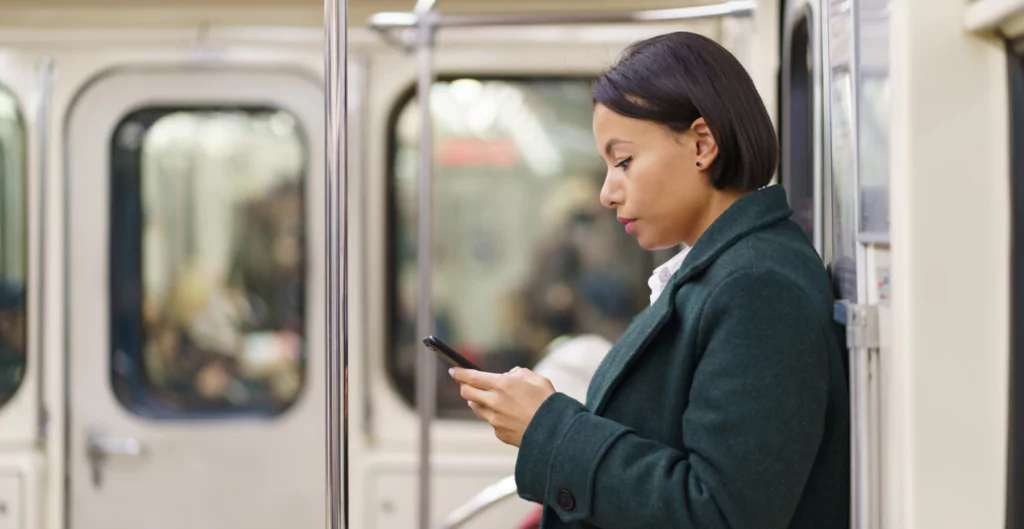 Mulher usando celular no metrô, simbolizando produtividade durante o deslocamento diário.