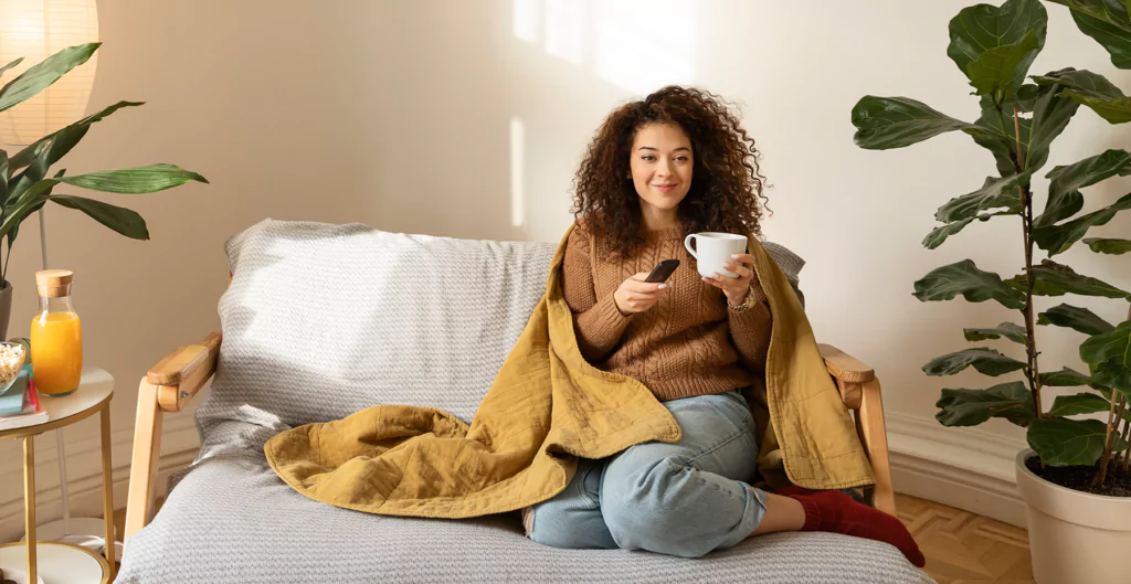 Mulher relaxando em casa com bebida quente, simbolizando dia de descanso.