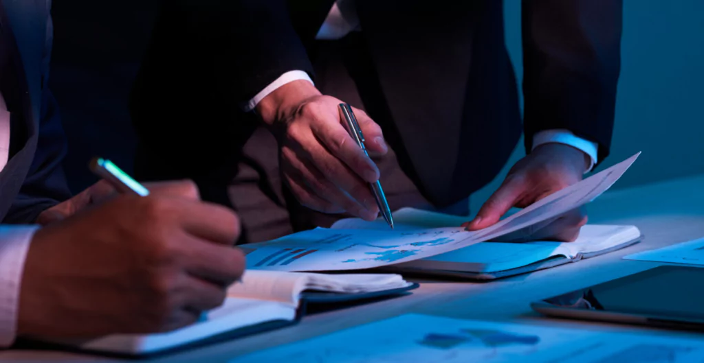 Duas pessoas analisando documentos e gráficos em uma reunião de negócios, focando em estratégias de planejamento.