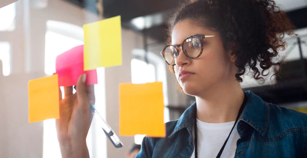 Mulher organizando ideias com post-its coloridos em um quadro.
