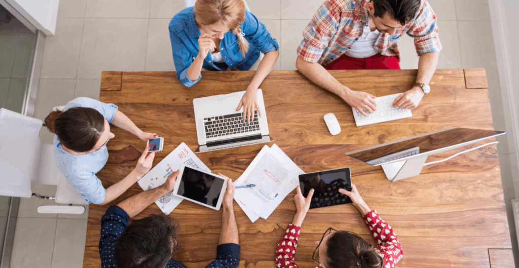 Equipe reunida com dispositivos, simbolizando flexibilidade no trabalho.
