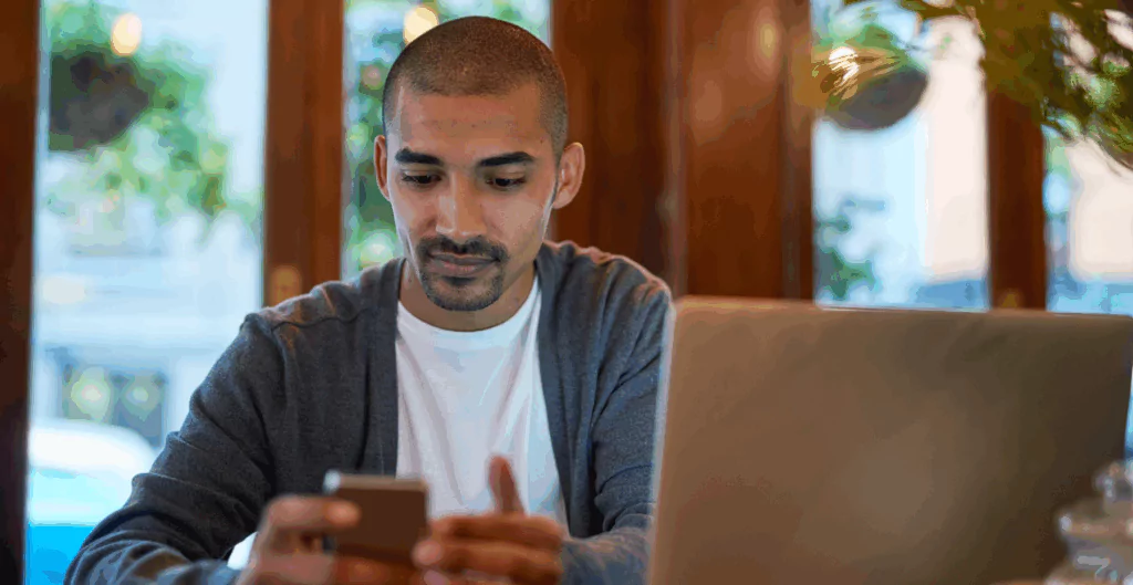 Homem com notebook e celular, representando comunicação de férias coletiva online.