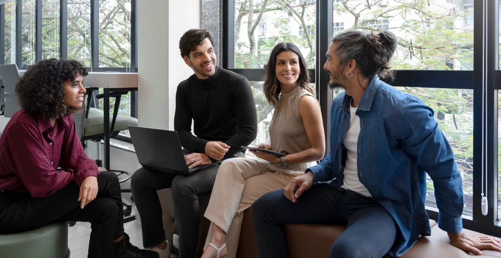 Quatro pessoas conversando de forma descontraída, com roupas sociais com escritório ao fundo